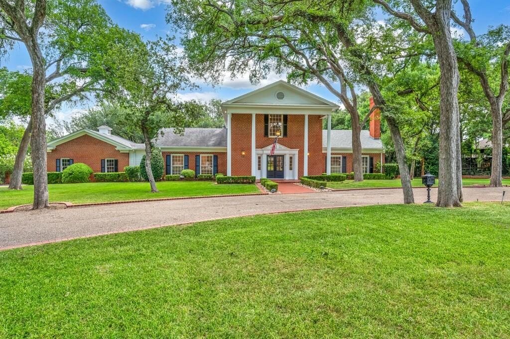 Brick colonial-style residence featuring a prominent columned portico and a gravel driveway