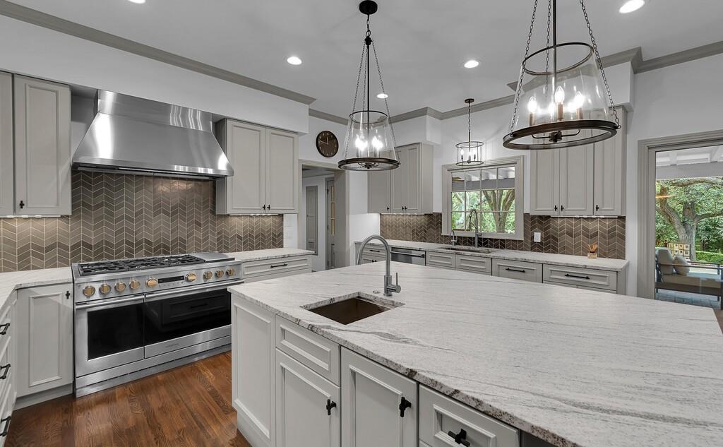 Gourmet kitchen featuring a large central island with an undermount sink, light-toned countertops, and custom cabinetry with dark hardware