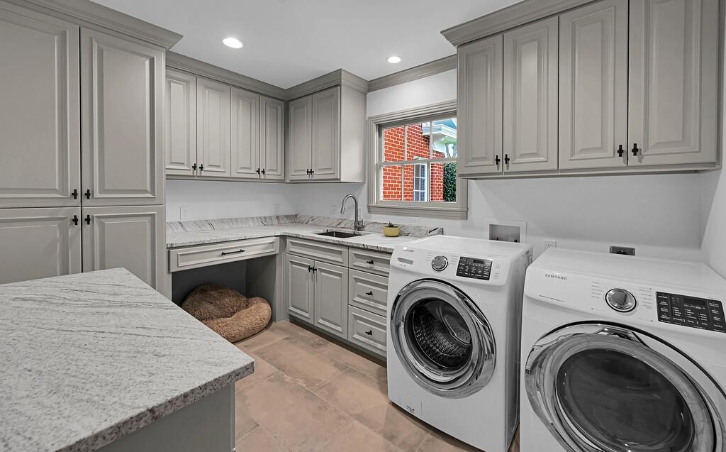 Laundry room featuring extensive built-in cabinetry, solid surface countertops, an undermount sink with a gooseneck faucet, and tile flooring