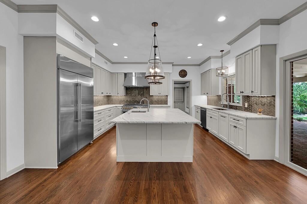 Spacious kitchen featuring a central island with a light-toned countertop, stainless steel appliances, light-toned cabinetry, a herringbone pattern backsplash, and wood-finish flooring