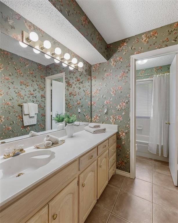 Bathroom featuring an extended single vanity with dual basins, wood-finish cabinetry, a white countertop, and a full-width mirror