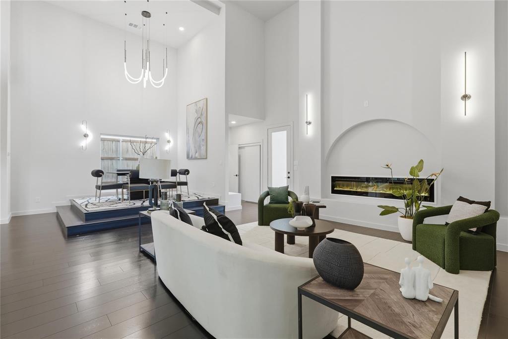 Open-concept living space with dark wood-finish flooring, soaring ceilings, a recessed linear fireplace, and a raised platform area