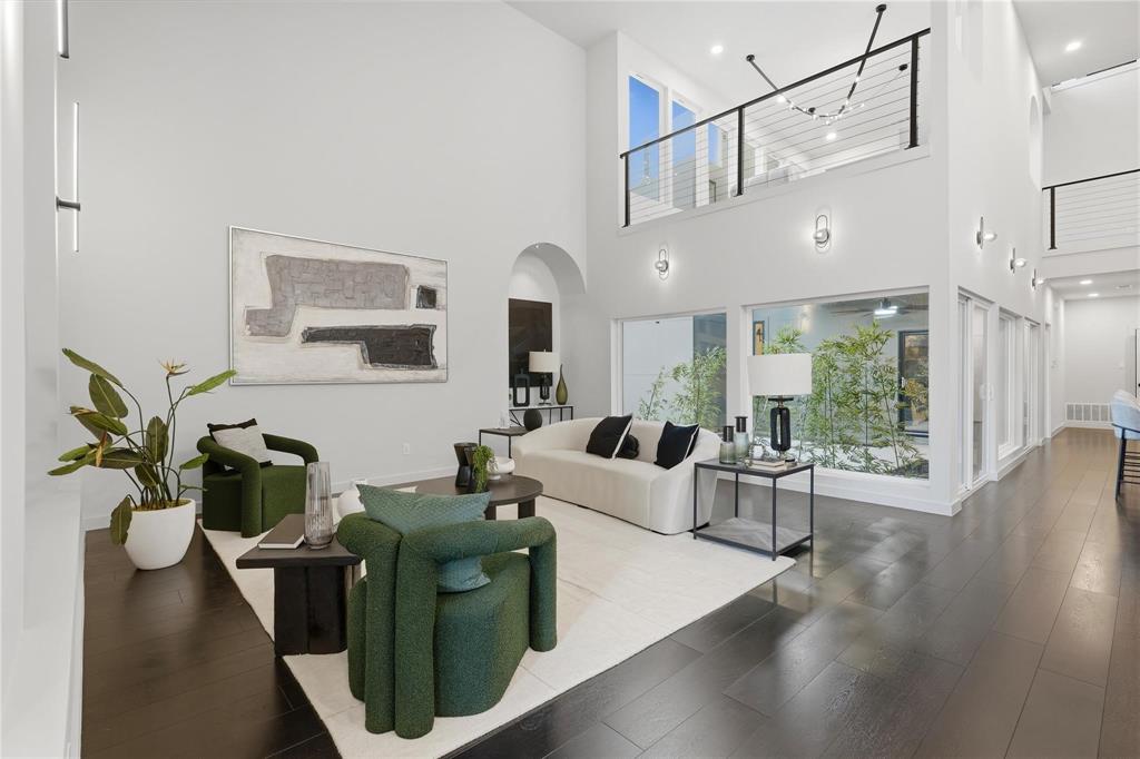 Double-height living space featuring dark wood-finish flooring, a contemporary staircase with cable railing, large windows with exterior foliage, and recessed lighting