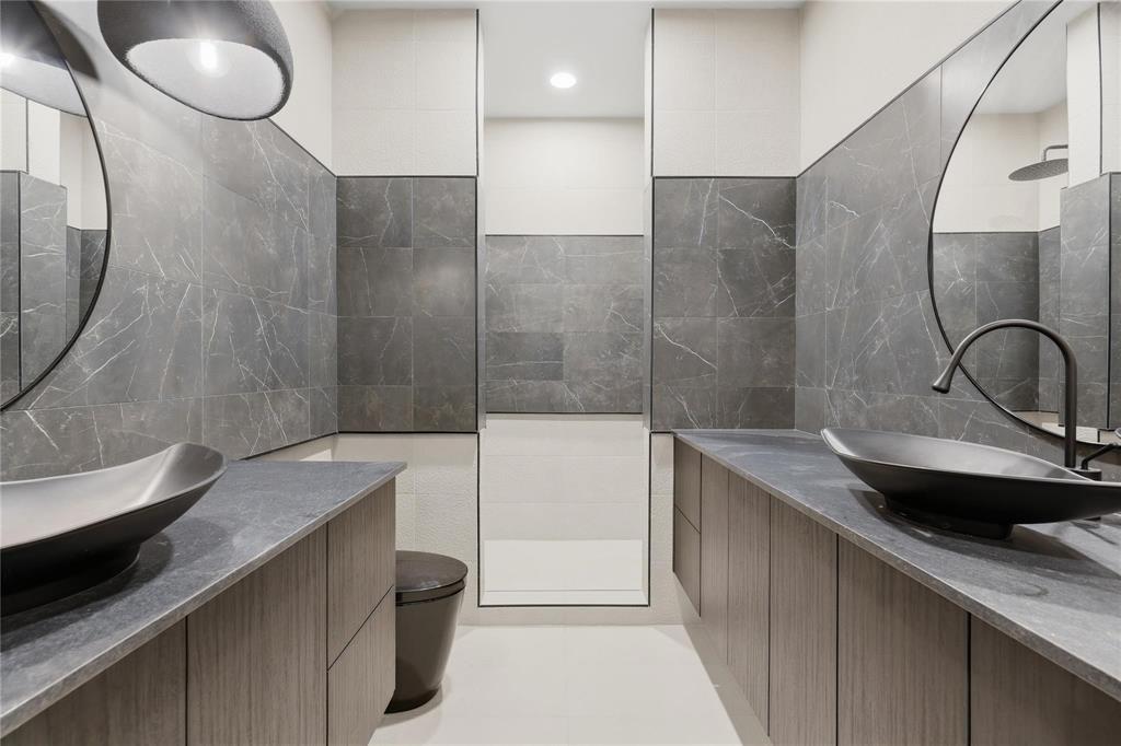 Dual floating vanities featuring wood-finish cabinetry, dark stone countertops, and vessel sinks with matte black fixtures