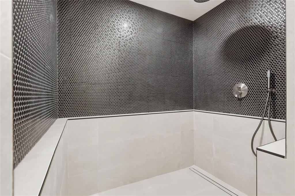 Shower enclosure featuring dark penny tile accent wall, light-toned large format ceramic wall tiles, recessed linear drain, brushed nickel shower controls, and a handheld showerhead