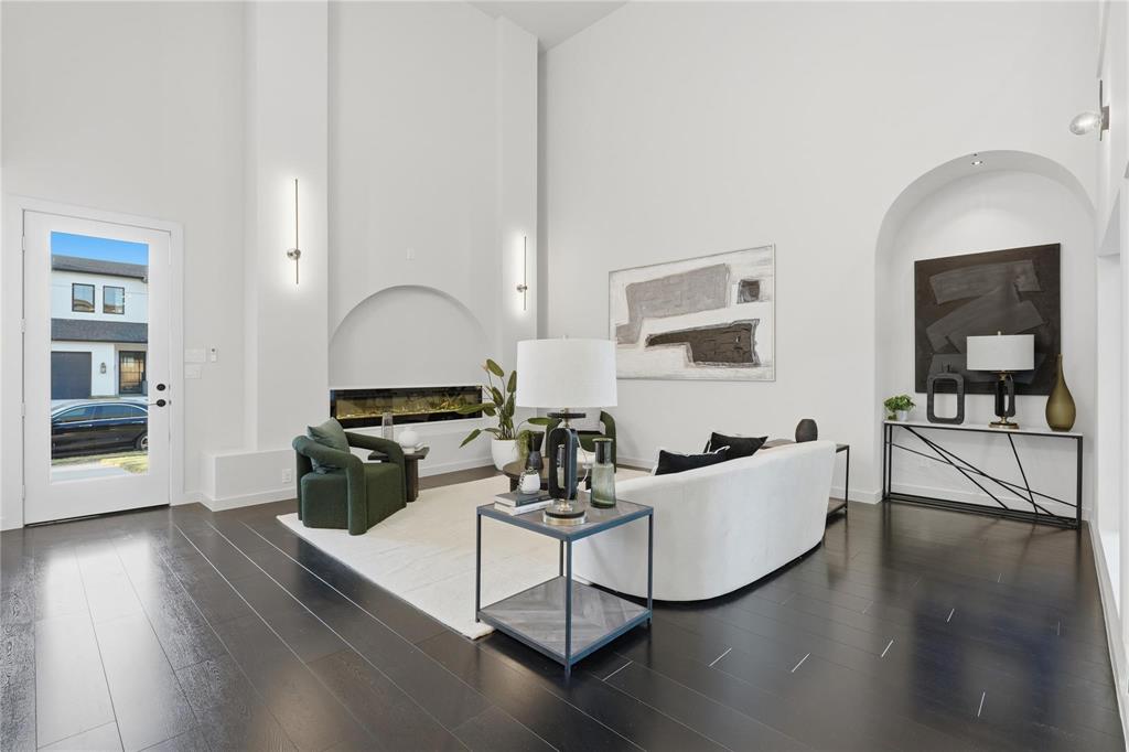 Spacious living area featuring high vaulted ceilings, dark wood-finish flooring, a modern horizontal fireplace, arched architectural details, and linear sconce lighting