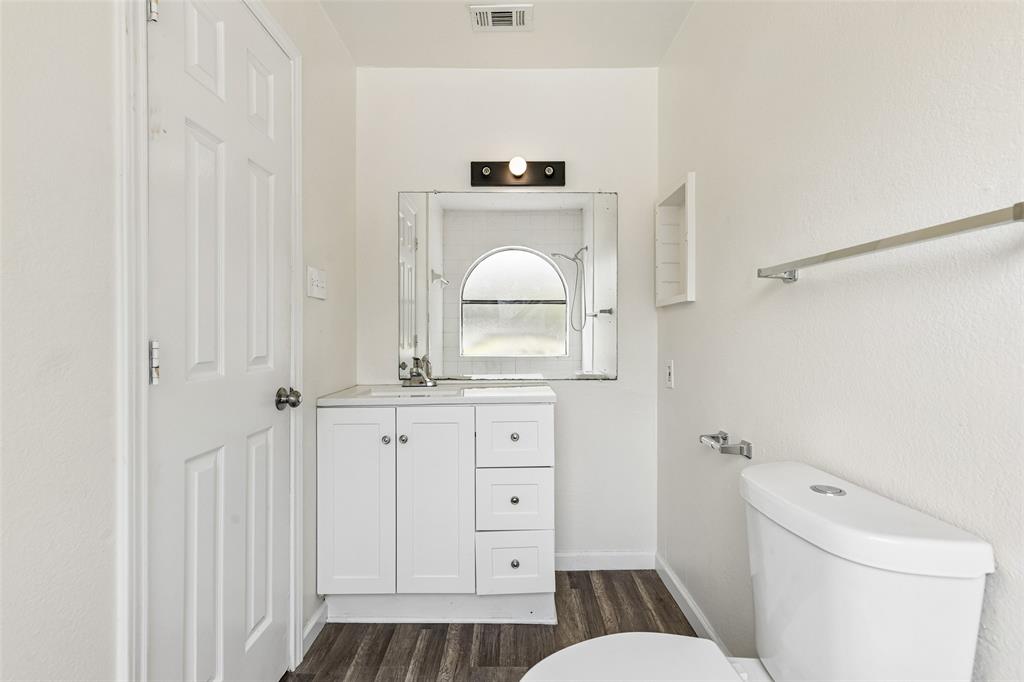 Bathroom featuring a white vanity with integrated sink, chrome faucet, wall-mounted mirror, and wood-finish flooring