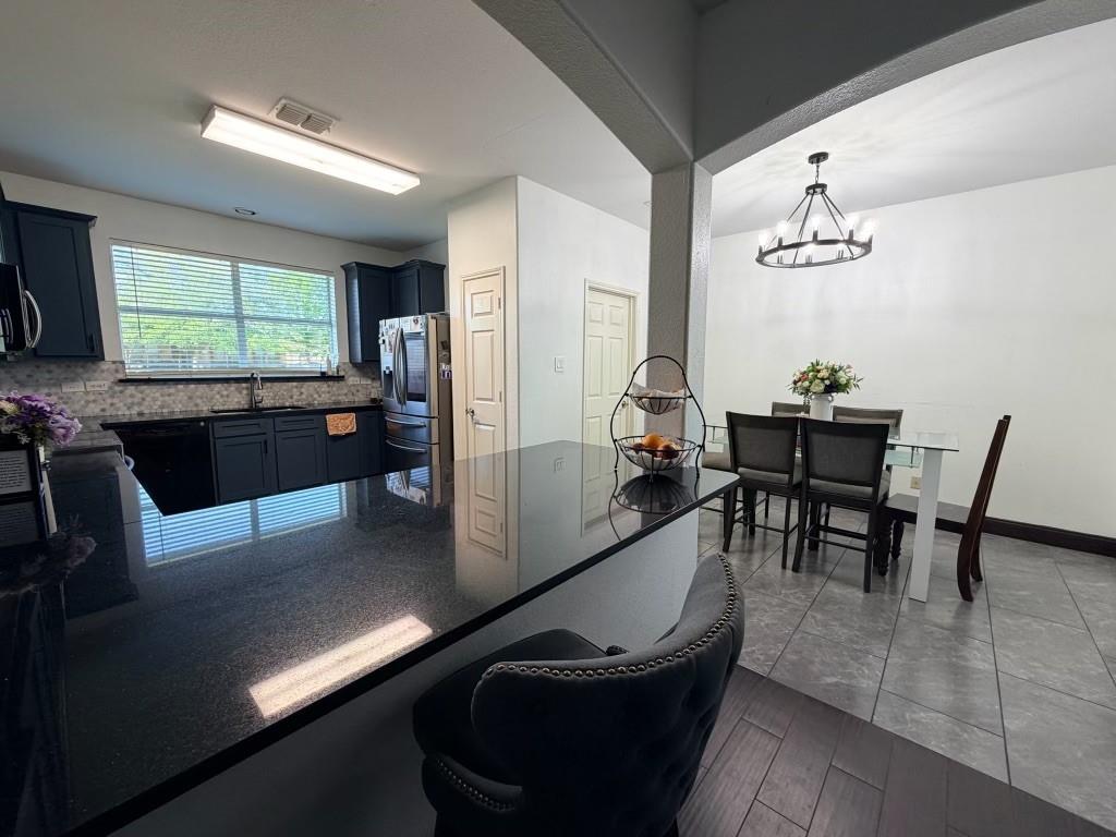 Kitchen featuring dark cabinetry, dark countertops, a tile backsplash, and a stainless steel refrigerator