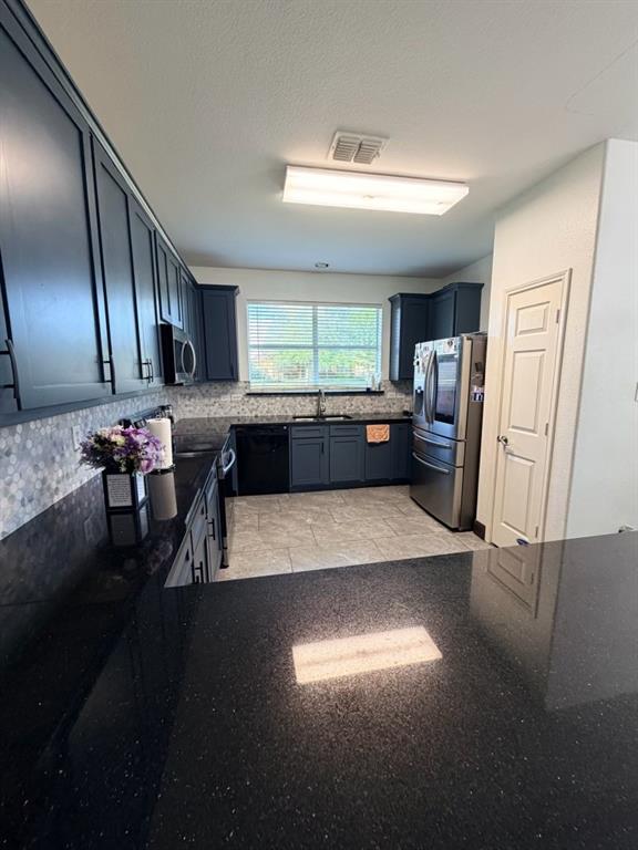 Modern kitchen featuring dark cabinetry, dark speckled countertops, a mosaic tile backsplash, stainless steel refrigerator, and recessed lighting