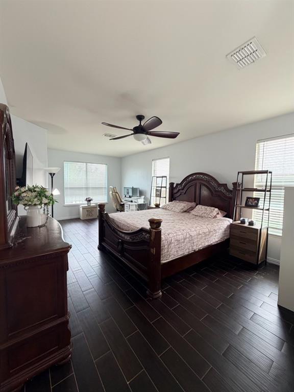 Spacious room featuring dark wood-finish flooring, a ceiling fan, and multiple windows with horizontal blinds