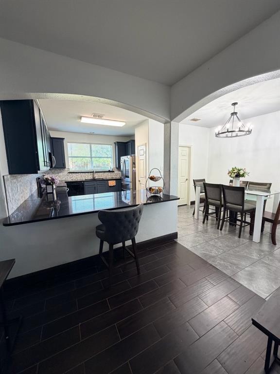 Open-concept kitchen and dining area featuring a breakfast bar with a dark countertop, dark wood-finish flooring, dark cabinetry, and an arched entryway to the dining space