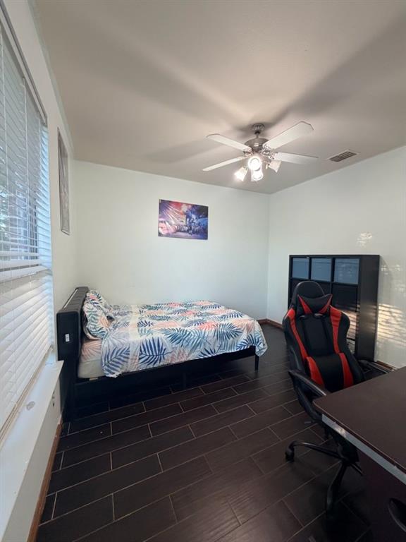 Spacious room featuring dark wood-finish flooring, a ceiling fan with integrated lighting, and multiple windows with blinds
