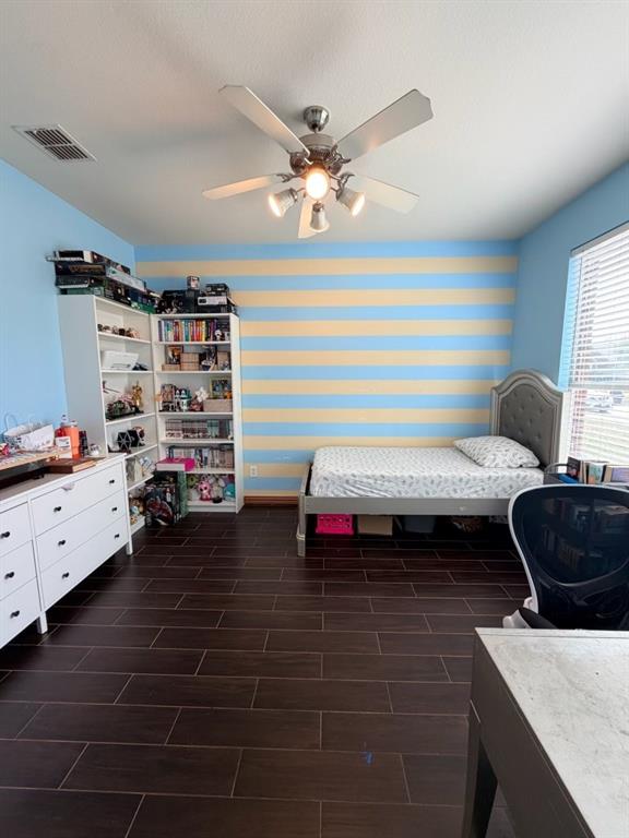 Spacious room featuring wood-finish flooring, a ceiling fan with integrated lighting, and a window with blinds