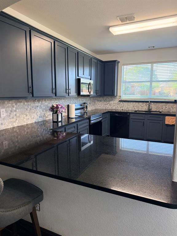 Kitchen featuring dark cabinetry with brushed nickel hardware, black countertops, and a mosaic tile backsplash