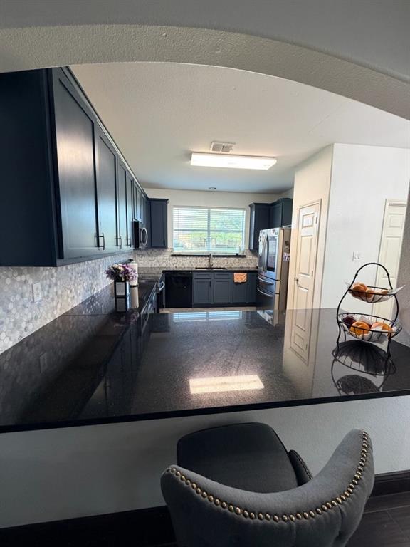 Kitchen featuring dark cabinetry, dark countertops, built-in appliances, and a mosaic tile backsplash