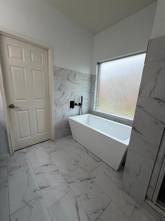 Updated Freestanding soaking tub with matte black fixtures, set against large format marble-look wall tile