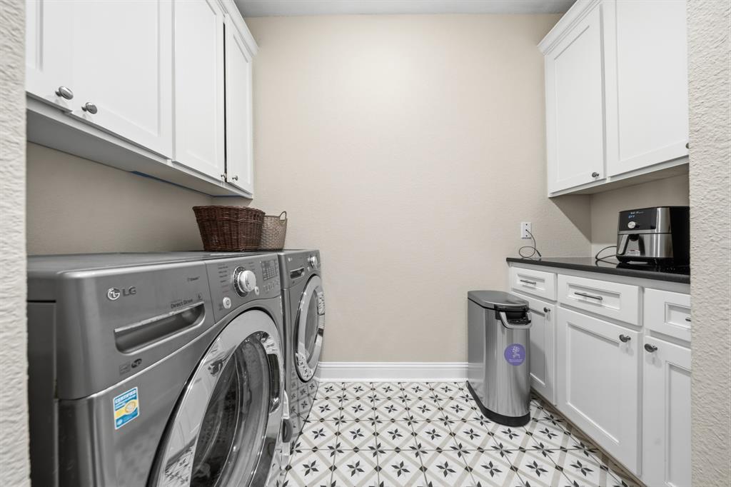 Laundry room featuring patterned floor tile, white shaker-style cabinetry, and dark countertops