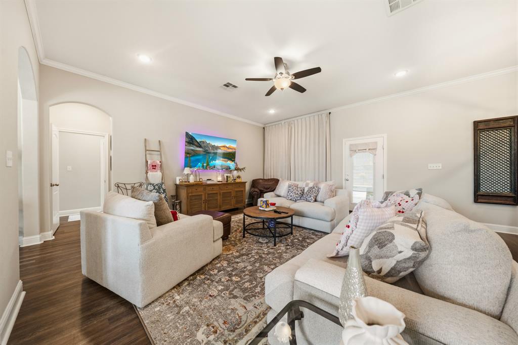 Living area featuring wood-finish flooring, an arched doorway, crown molding, a ceiling fan with integrated lighting, and recessed lighting