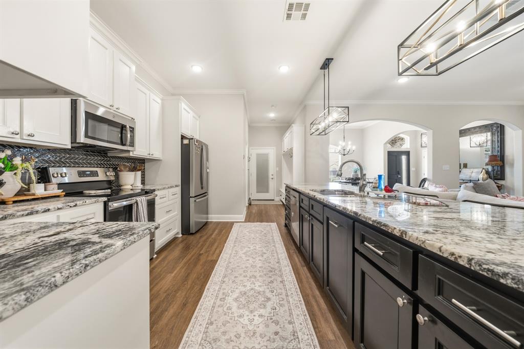 Kitchen featuring an expansive island with a light-toned countertop, stainless steel appliances, white upper cabinetry, dark lower cabinetry, and wood-finish flooring