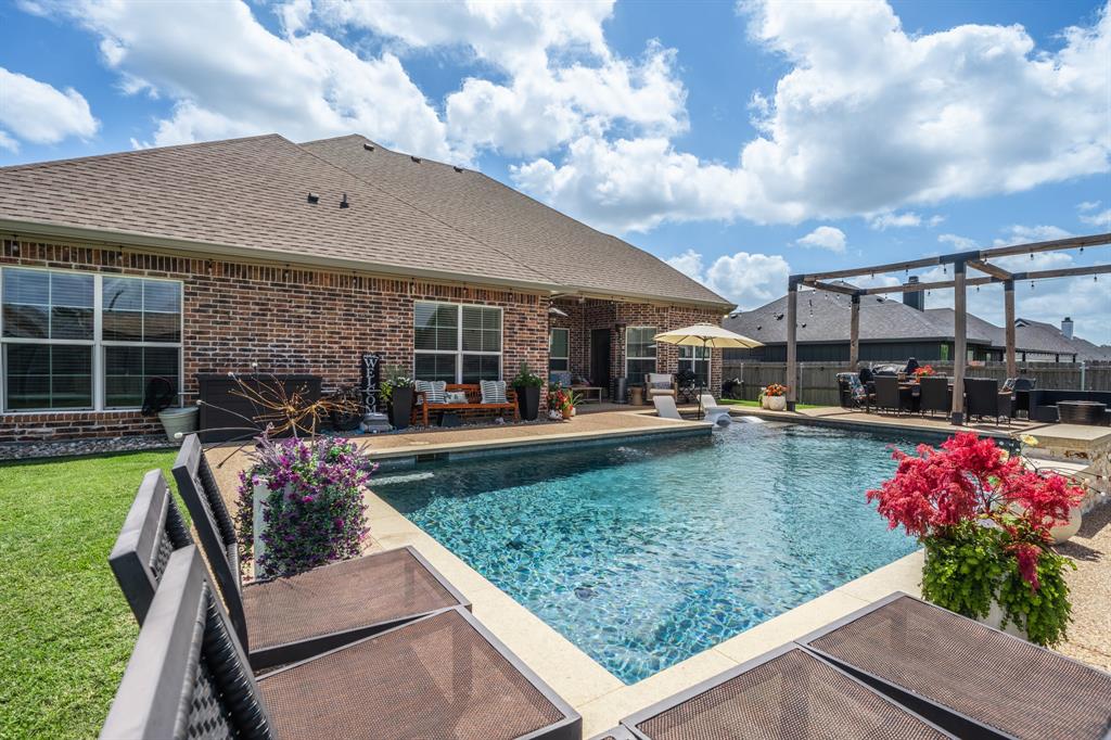 Spacious backyard featuring a rectangular swimming pool with surrounding patio, a brick exterior, and a large pergola structure