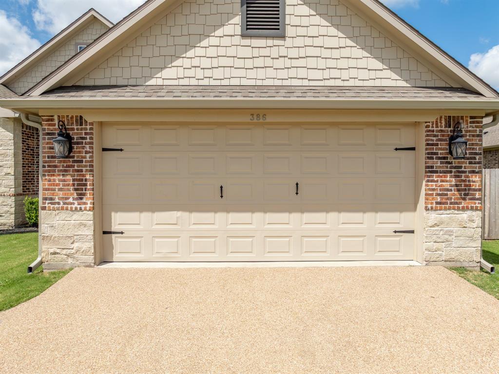 Front exterior featuring a multi-tone brick and stone facade, shake siding, an integrated garage with decorative hardware, and a textured aggregate driveway
