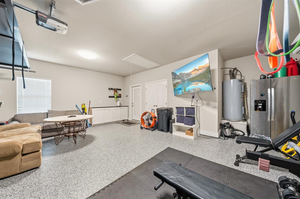 Spacious garage with light gray speckled epoxy flooring, white built-in cabinetry with a dark countertop, overhead garage door opener, and a single window with blinds