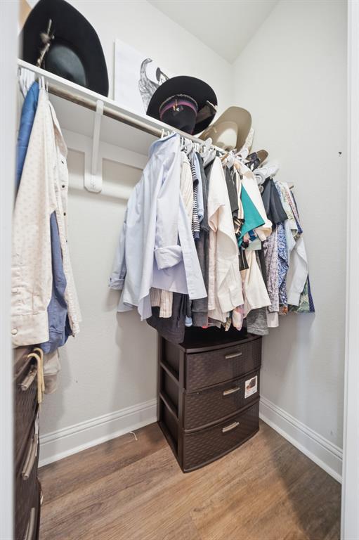 Compact closet space featuring a single hanging rod, upper shelving, and wood-finish flooring