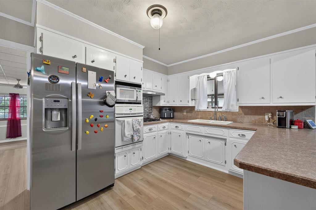 Kitchen featuring wood-finish flooring, white cabinetry, a built-in oven, and a stainless steel refrigerator