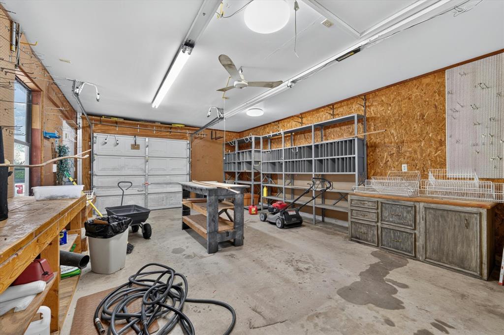Spacious garage featuring a concrete floor, multiple built-in shelving units, a workbench, and integrated overhead lighting