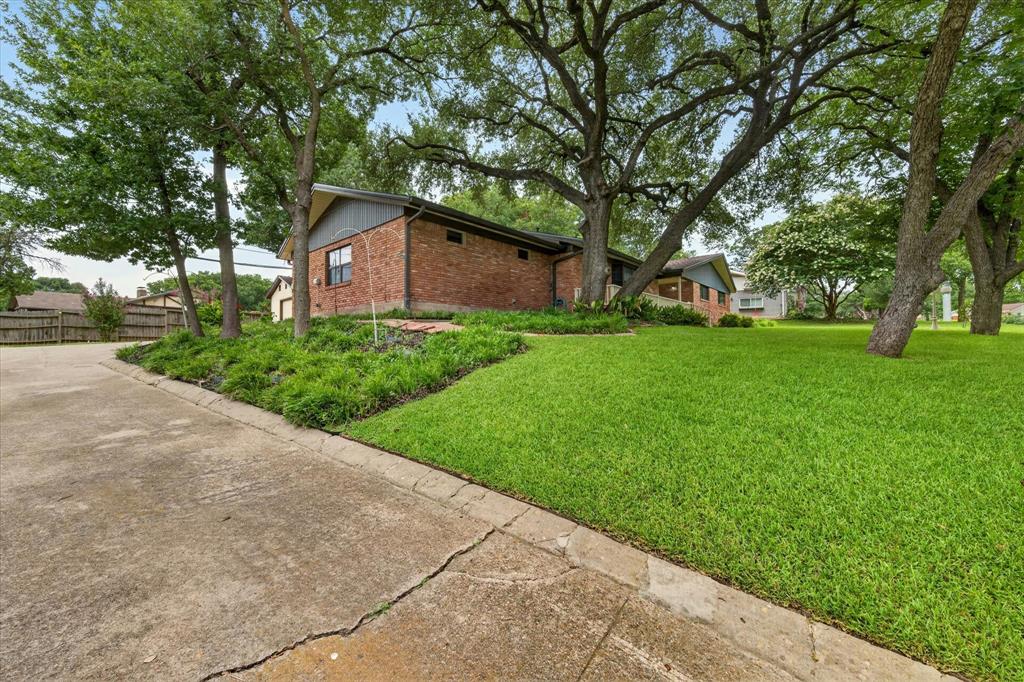 Brick exterior with a gabled roofline, mature trees, landscaped shrubbery, and an expansive lawn area Brick exterior with a gabled roofline, mature trees, landscaped shrubbery, and an expansive lawn area