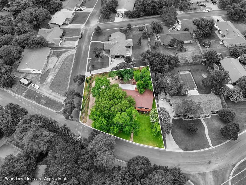 Aerial perspective showcasing a corner lot with mature trees, a red-toned roof, and a verdant lawn Aerial perspective showcasing a corner lot with mature trees, a red-toned roof, and a verdant lawn