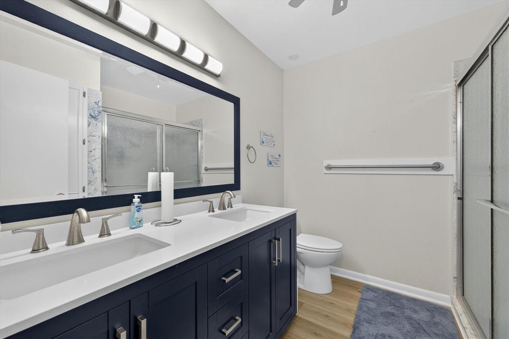Dual-sink vanity with a white countertop and navy cabinetry, brushed nickel hardware, a framed mirror, and a glass-enclosed shower