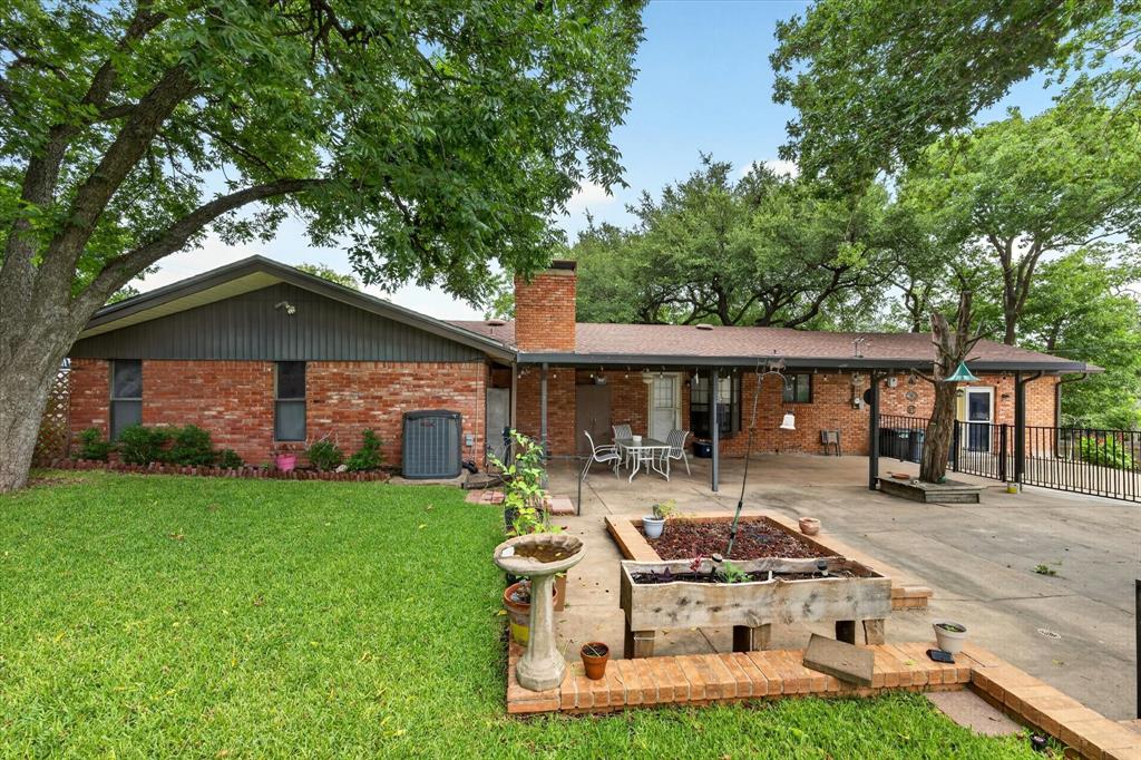 Brick exterior featuring a covered patio, a spacious concrete pad, a raised planter, and mature trees providing natural shade
