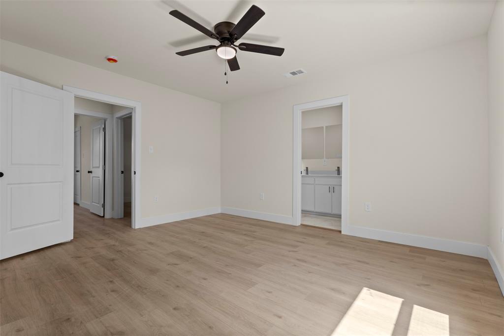 Light wood-finish flooring, white walls, dark ceiling fan with integrated lighting, and white interior doors with dark hardware