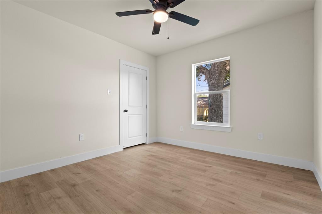 Wood-finish flooring, neutral wall tones, ceiling fan with light, white trim, and a paneled door