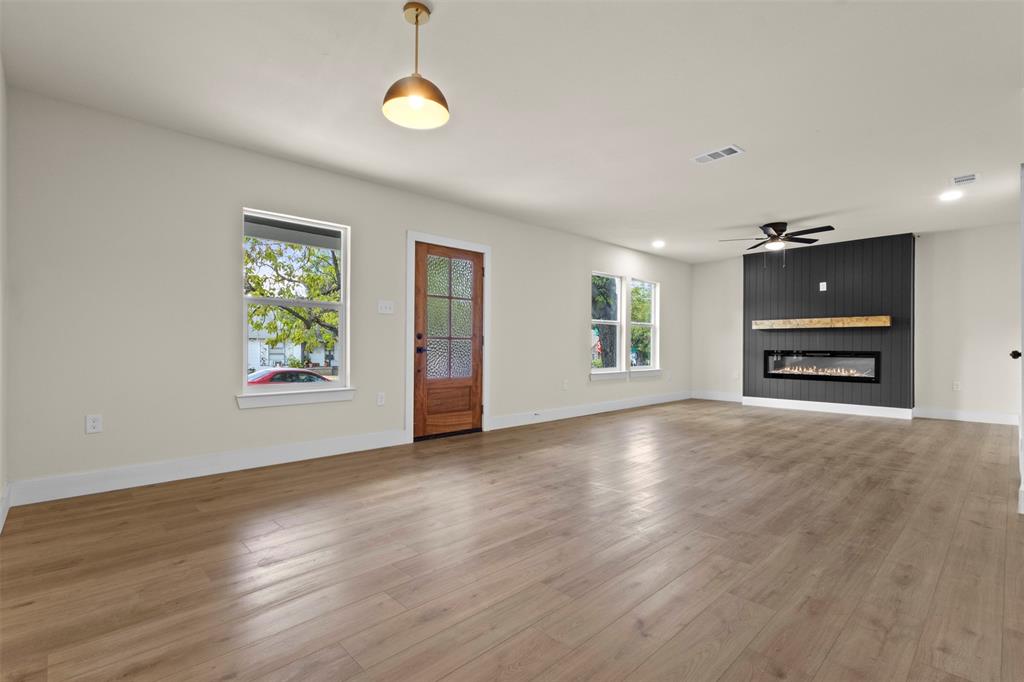 Expansive living area featuring light wood-finish flooring, a modern linear fireplace with a wood mantel, a black vertical slat accent wall, and recessed lighting