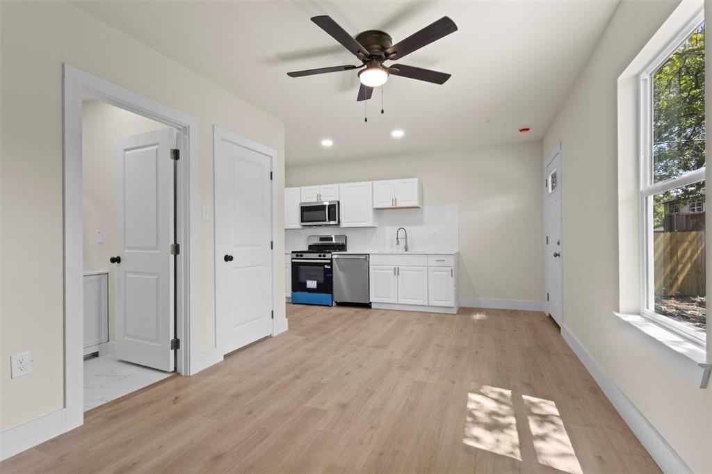 Open-concept living space with wood-finish flooring, a contemporary ceiling fan, and white kitchen cabinetry