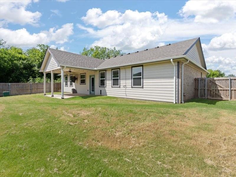 Expansive backyard featuring a covered patio, ceiling fan, and privacy fencing