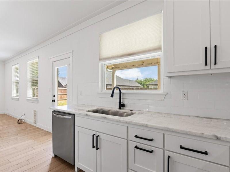 Kitchen area featuring white shaker cabinetry with black hardware, a stainless steel sink, and a black gooseneck faucet