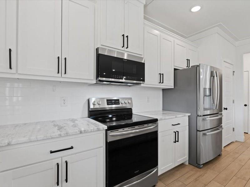 Kitchen featuring white shaker-style cabinetry with matte black hardware, stainless steel appliances, a subway tile backsplash, and light-toned countertops