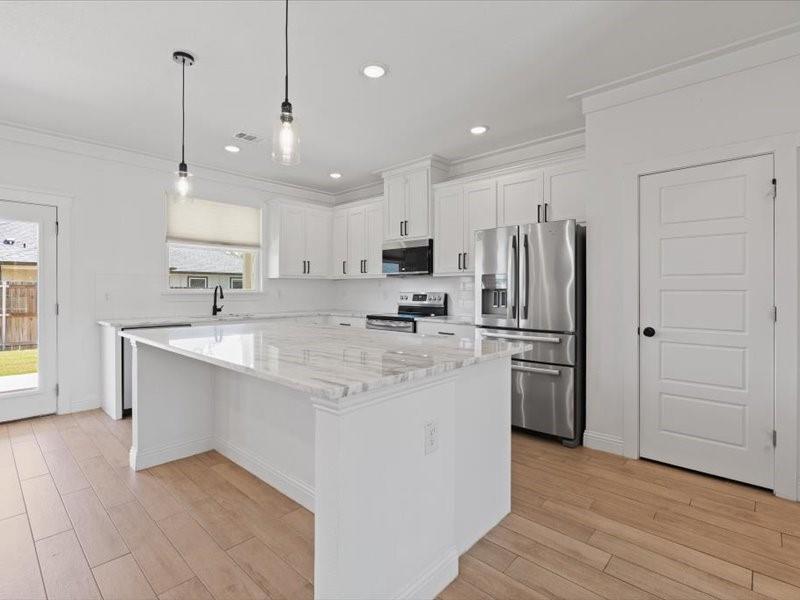 Modern kitchen featuring an expansive center island with a stone countertop, white shaker cabinetry, stainless steel appliances, and wood-finish flooring