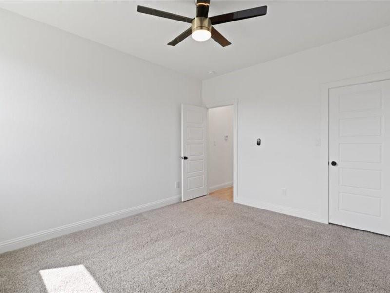 Spacious room featuring light gray carpet, white baseboards, and a modern ceiling fan with integrated lighting