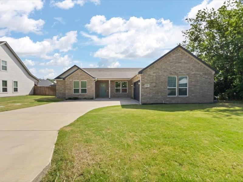 Brick veneer exterior with a contrasting teal entry door, a multi-car concrete driveway, a gabled roofline, and an integrated garage Brick veneer exterior with a contrasting teal entry door, a multi-car concrete driveway, a gabled roofline, and an integrated garage