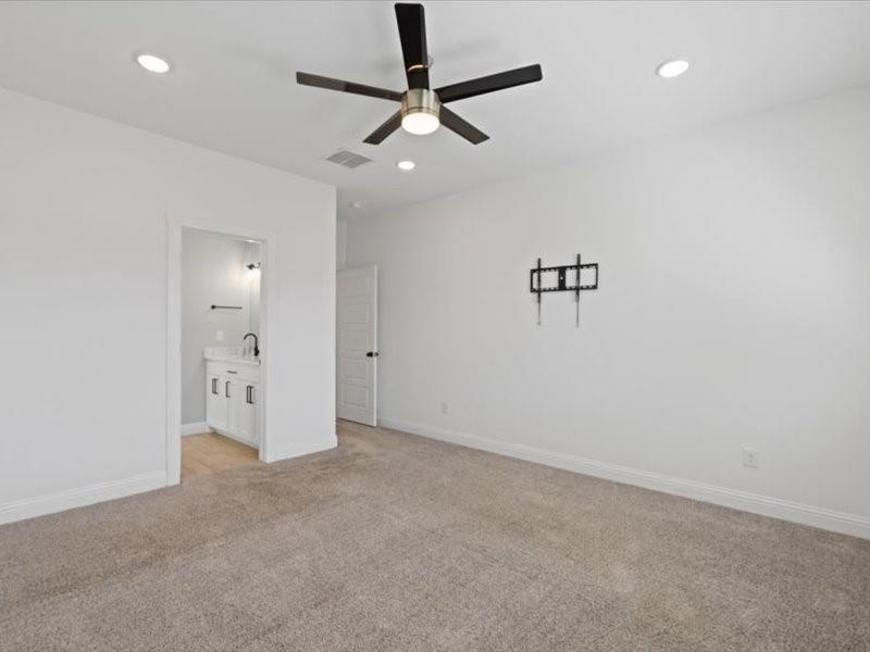 Spacious carpeted room featuring a ceiling fan with integrated lighting, recessed lighting, and a doorway revealing a vanity with a dark faucet and a wall-mounted towel rack