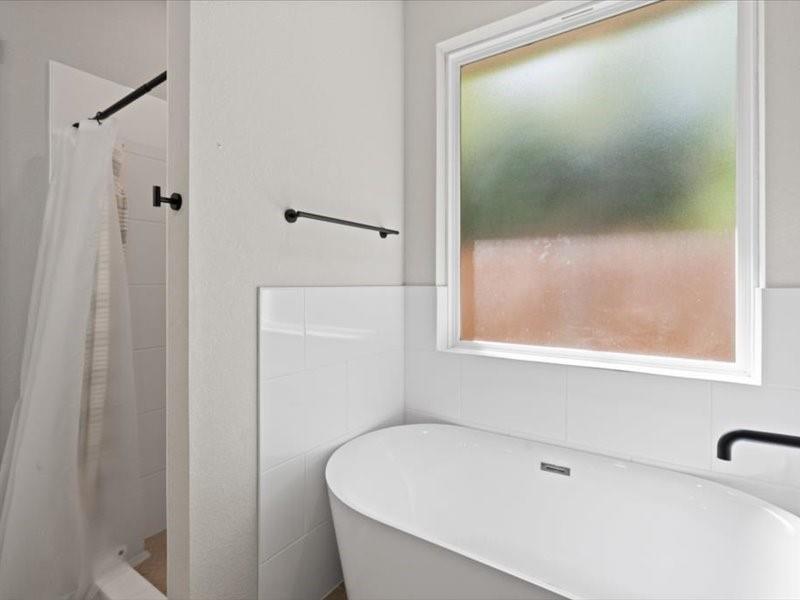 Freestanding soaking tub with a matte black wall-mounted faucet, complemented by a white tiled wall surround and a frosted window
