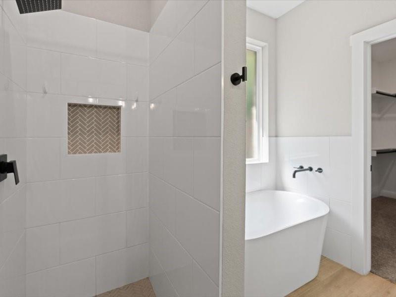 Shower with white subway tile surround and a herringbone-patterned tile niche, complemented by a freestanding soaking tub with wall-mounted matte black fixtures