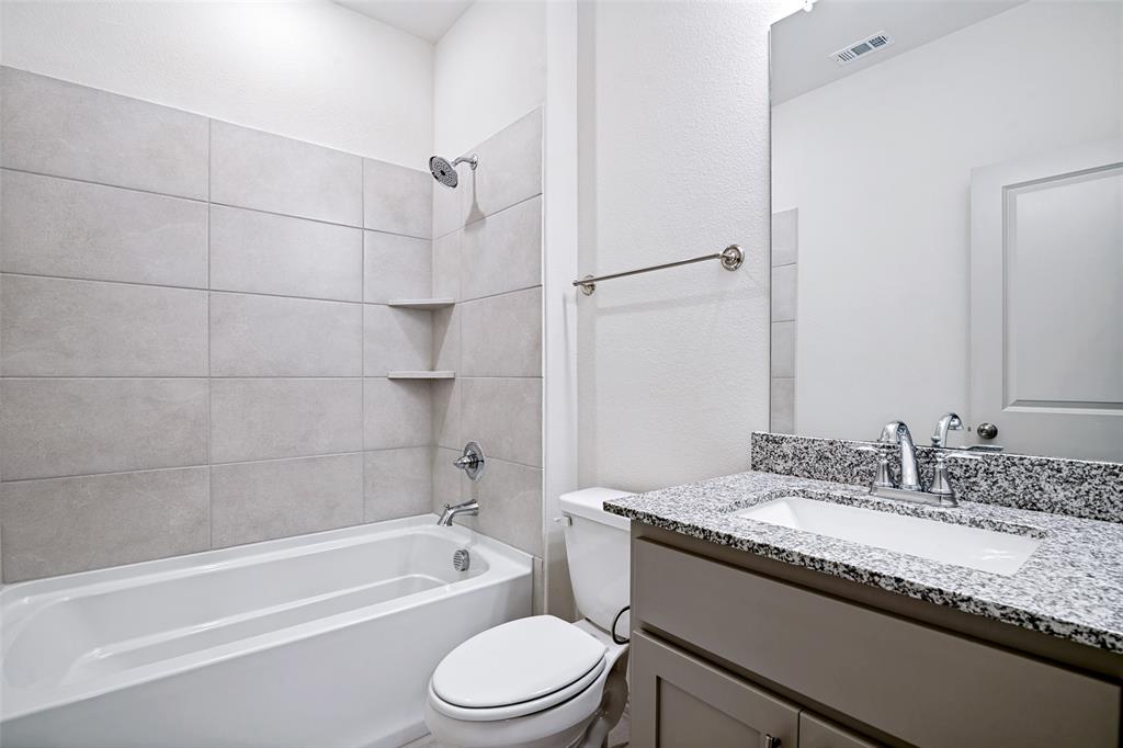 Bathroom featuring a bathtub with tiled surround and integrated shelving, granite-finish countertop, under-mount sink, and chrome fixtures