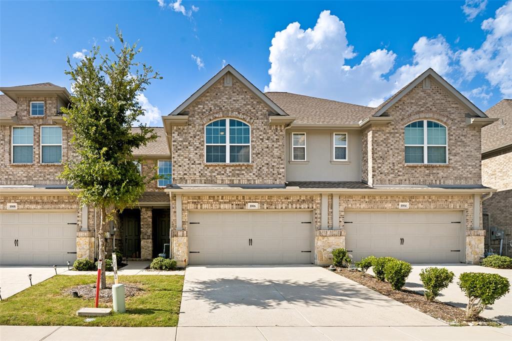 Brick facade townhouse featuring an attached garage, arched window, and mature landscaping Brick facade townhouse featuring an attached garage, arched window, and mature landscaping