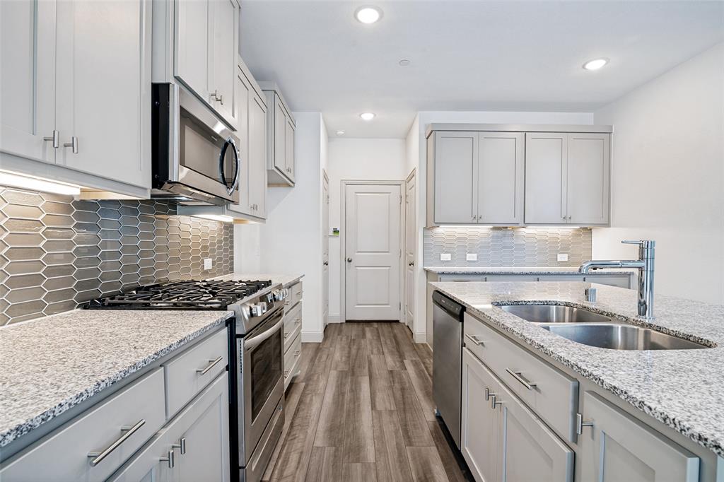 Modern kitchen featuring light gray cabinetry with brushed nickel hardware, granite countertops, stainless steel appliances, a gray picket tile backsplash, and wood-finish flooring