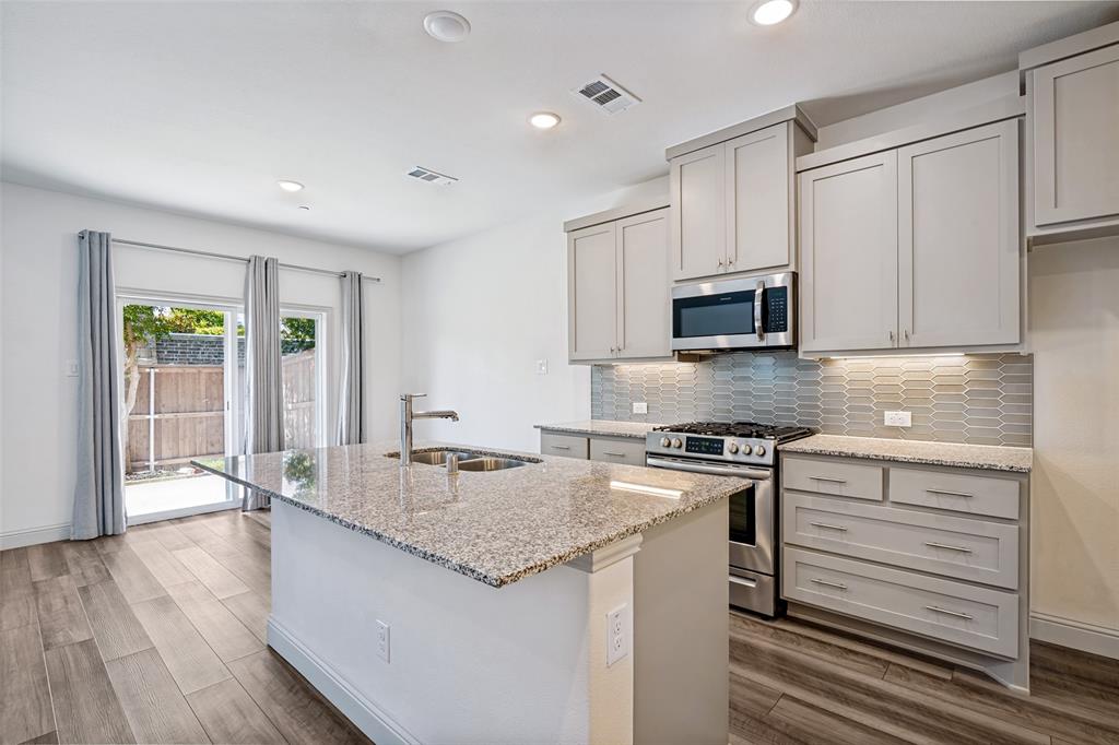 Modern kitchen featuring an island with a double basin sink, granite countertops, and stainless steel appliances